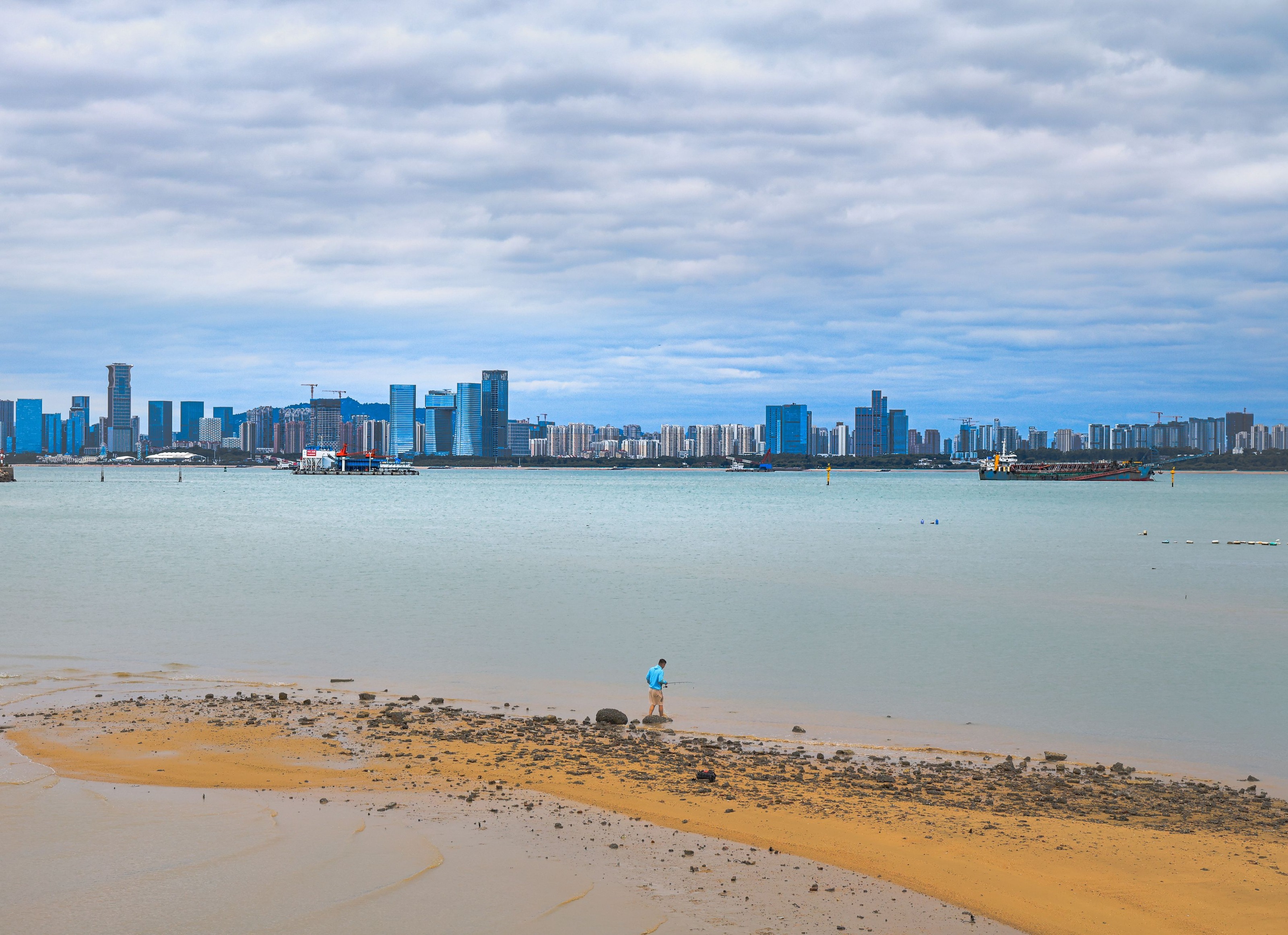 海口海岸高清实景,海湾对面的城市天际线与海边的人